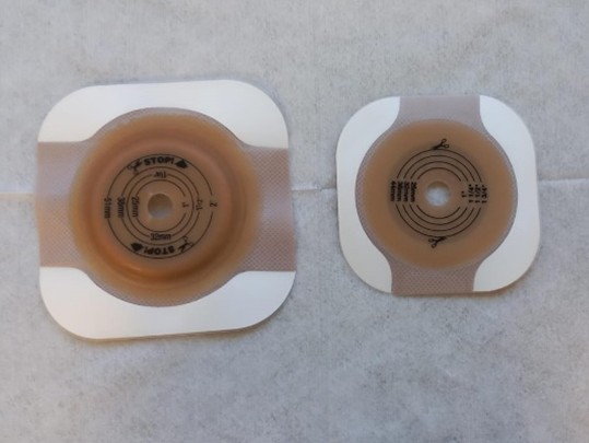 Imagem de barreiras cutâneas circulares usadas para fixação de bolsas de colostomia no abdômen do paciente Duas bases adesivas para bolsa de colostomia de tamanhos diferentes sobre uma superfície clara