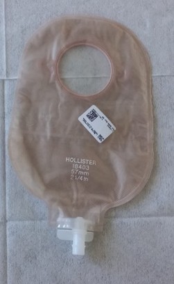 Bolsa de colostomia da marca Hollister, modelo 18403, com abertura circular superior e saída inferior com válvula branca. A bolsa é translúcida e possui uma etiqueta com código de barras colada.